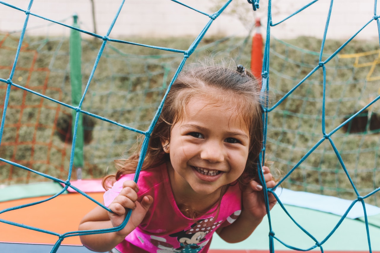 Young girl smiles while poking head through playground netting